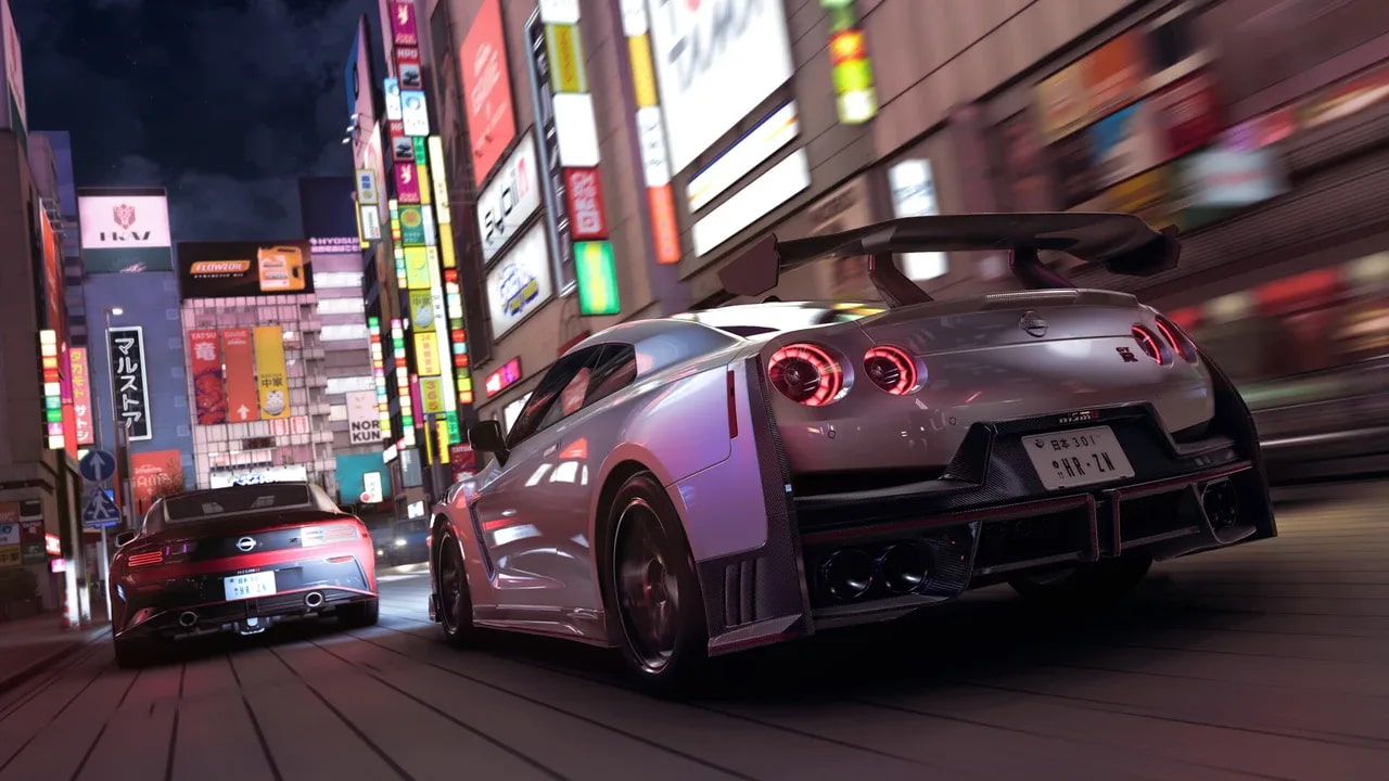 Two Nisan cars drive through Tokyo at night. Neon lights illuminate the city streets around the vehicles.